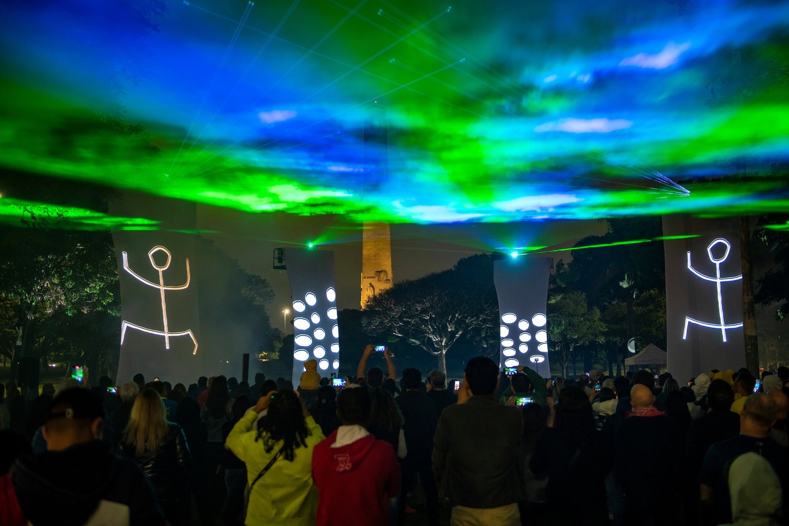 Público assistindo a projeções mapeadas e lasers verdes durante o Festival de Luzes