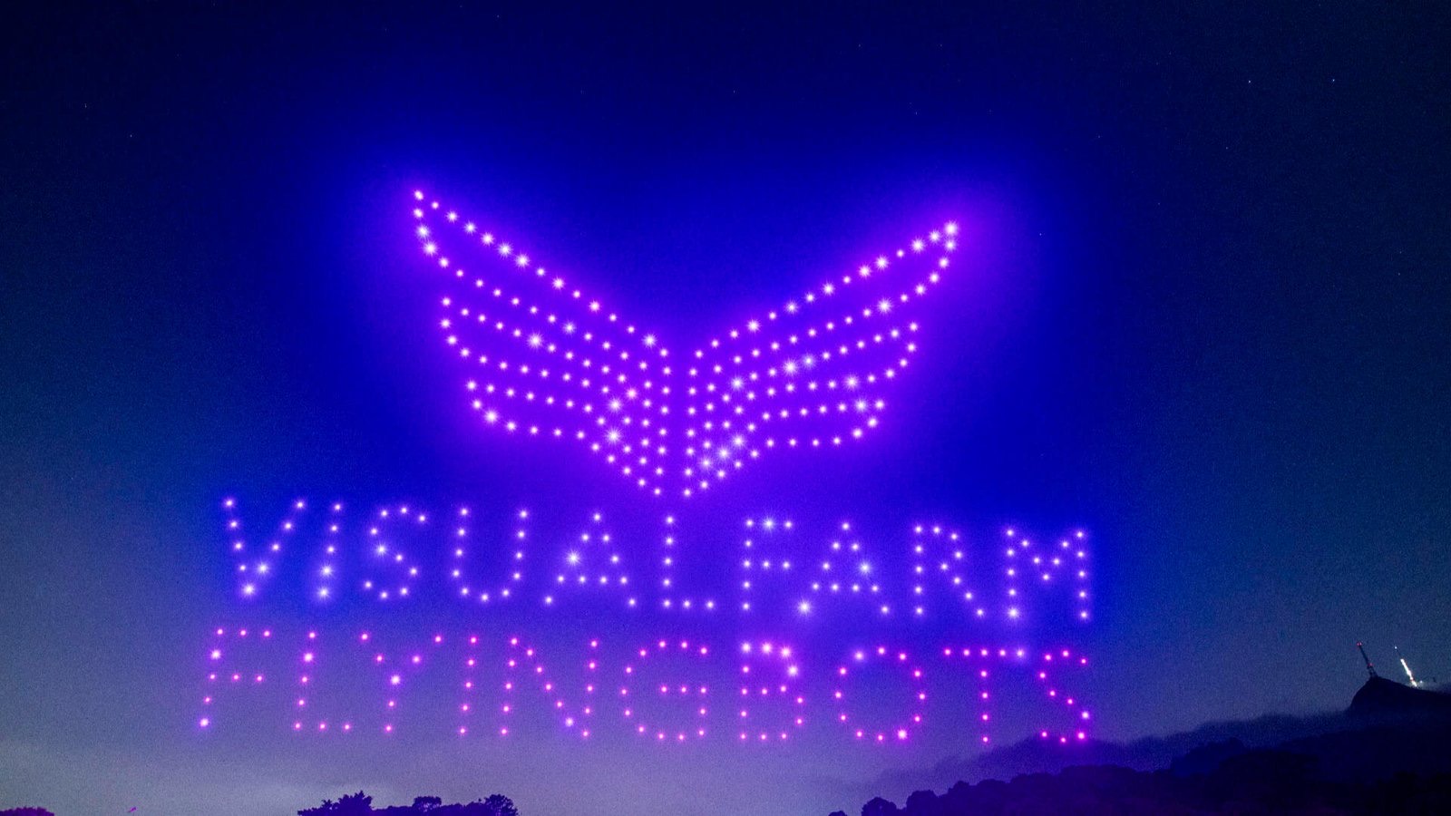 Centenas de drones da Visual Farm formando o logotipo e a palavra Flyingbots no céu noturno